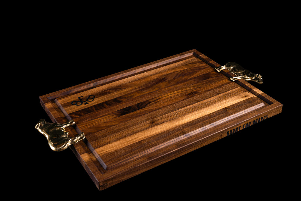 Tomahawk board in walnut at an angle, groove side up with two brass Bull handles and Burnt End Boards branded on the edge